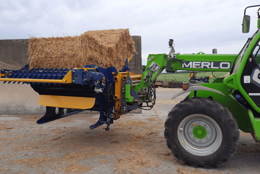 Un tracteur Merlo vert soulève un grand ballot de paille dans une dérouleuse-pailleuse DE450RPH